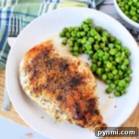 Grilled chicken breast with pepper and herbs, perfectly cooked on the stove, served with peas on a white plate, next to a blue plaid napkin.