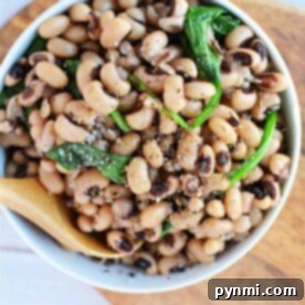 A wooden spoon rests on a bowl of seasoned black-eyed peas with spinach, inviting you to savor its flavor. Wondering how long to cook black-eyed peas? Perfectly tender in just about an hour, they make a delicious and wholesome meal on any wooden surface.