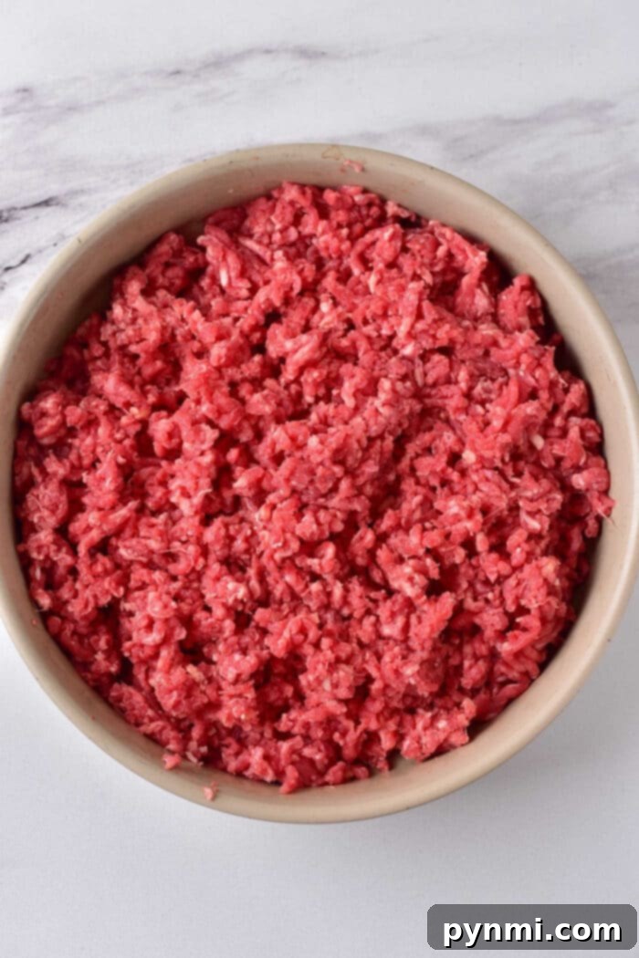 Perfect Ground Beef Every Time: Your Cooking Guide 3 A bowl filled with raw ground meat rests on a marble surface, inviting you to ponder how long to cook ground beef for the perfect savory dish.