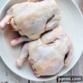 Two whole uncooked cornish hens rest on a white plate against a rustic wooden background, inviting the question: how long to cook Cornish hens to achieve that perfect balance of tenderness and flavor?.