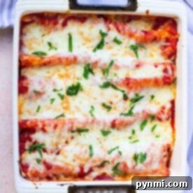 Baked enchiladas topped with melted cheese and fresh herbs in a square dish on a striped cloth, perfectly done after cooking to perfection.