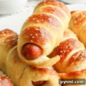 Soft pretzel-wrapped hot dogs stacked on a plate, with ketchup and mustard in bowls in the background—perfect for anyone wondering how long to cook pigs in a blanket for that golden, delicious finish.