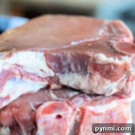 Close-up of two raw pork chops stacked on a plate, waiting to reveal their succulent flavors once you know how long to cook bone-in pork chops perfectly.