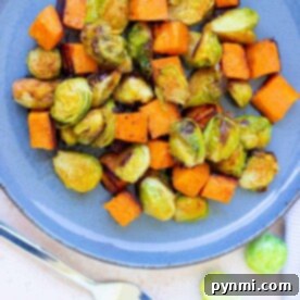 A delicious plate featuring perfectly roasted Brussels sprouts and sweet potatoes sits invitingly, with a fork poised beside it, ready to dive into this wholesome delight.
