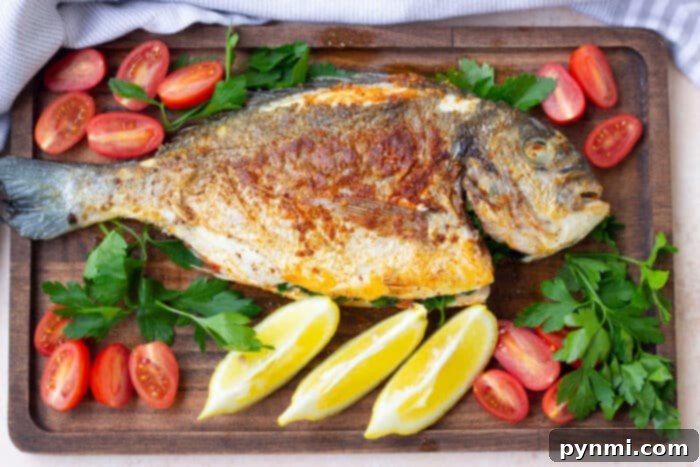 Perfectly cooked whole fish garnished with lemon, tomatoes, and parsley on a wooden board.