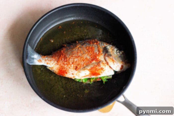 A whole pan-fried fish in a skillet, showcasing a golden, crispy skin.