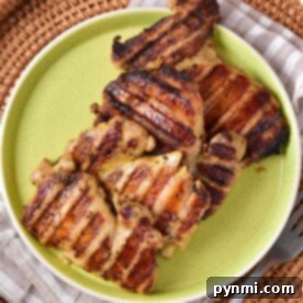 Grilled chicken pieces, expertly cooked to perfection, are served on a green plate resting on a checkered cloth placed upon a wicker tray. Wondering how long to grill chicken thighs for the juiciest flavor? This delightful scene holds the delicious secret!.