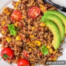 Tri Color Quinoa salad with cherry tomatoes, corn, avocado slices, and a fork elegantly displayed on a white plate.