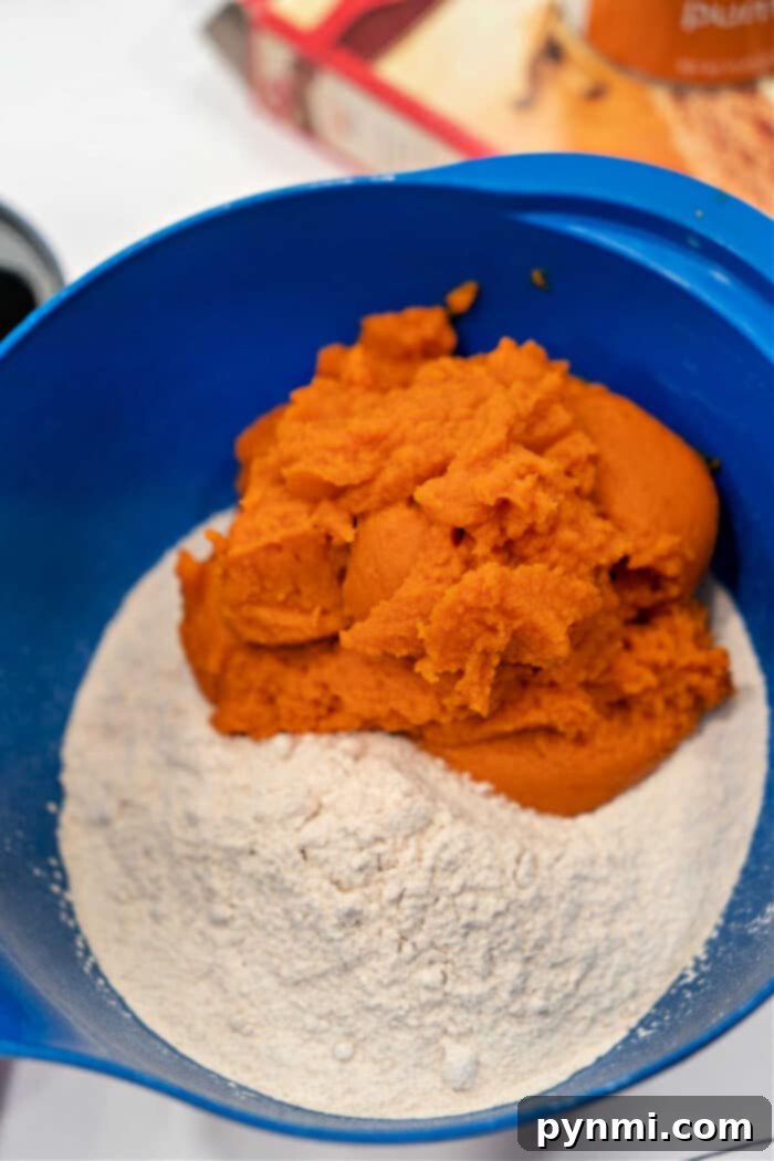 A blue mixing bowl containing a rich orange batter, a perfect blend of cake mix and pumpkin puree for baking.