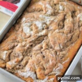 A freshly baked coffee cake made with yellow cake mix sits in a rectangular pan, dusted with sugar beside the box.