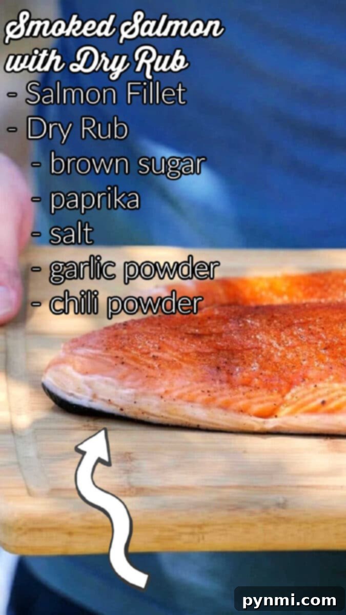 A close-up of a hand holding a wooden board with a seasoned Coho salmon fillet. Text overlay lists ingredients: “Smoked Salmon with Dry Rub - Coho Salmon Fillet, Dry Rub, brown sugar, paprika, salt, garlic powder, chili powder." A curved arrow points to the fillet.