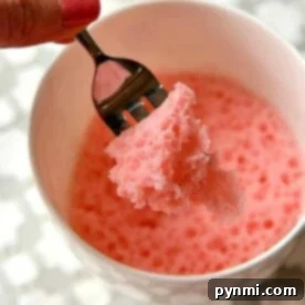 Effortless Cake Mix Mug Cake 7 A hand holding a fork with pink mug cake over a white bowl showcases how to make a delightful treat using cake mix.