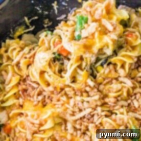 Creamy Slow Cooker Chicken Noodle Delight 7 Close-up of a cheesy slow cooker chicken casserole with noodles, vibrant vegetables, and crispy fried onions in a black dish.