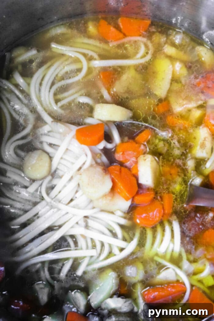 How to Make Pho Broth - A straining process for pho broth, showing clear broth being poured through a fine-mesh strainer into another pot.