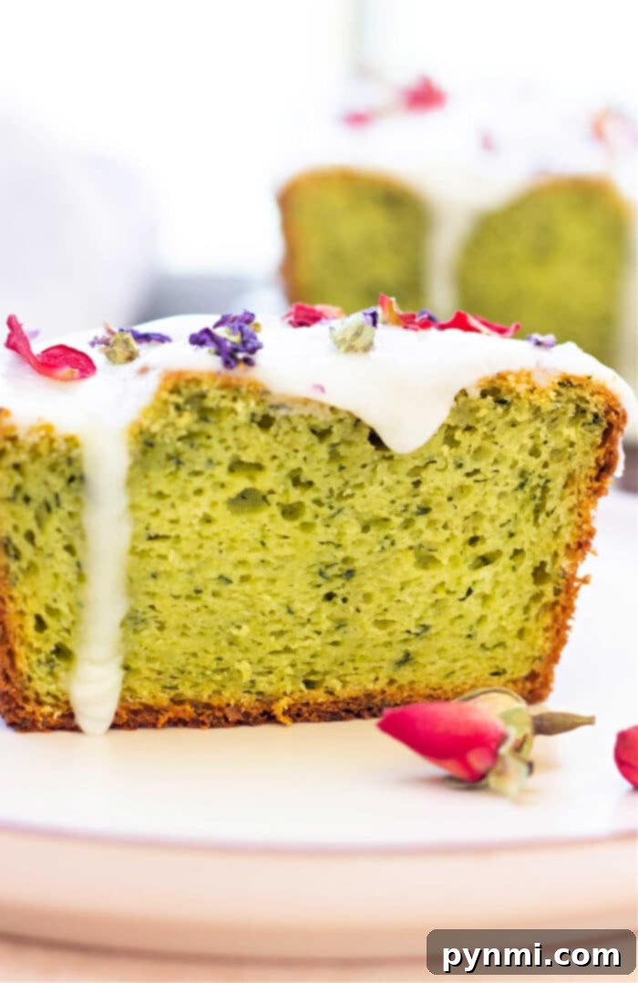 Green Goddess Avocado Cake 2 A beautifully sliced piece of moist avocado cake with a creamy white powdered sugar glaze and delicate dried flower petals, elegantly presented on a plate.
