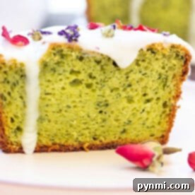 Close-up of a avocado cake slice with white icing and dried flower petals on top, complemented by rosebuds nearby, artfully reminiscent of an avocado cake.