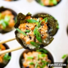 Salmon Sushi Bites 7 Close-up of a salmon sushi cup bite with seaweed, rice, and toppings, held by chopsticks over a muffin tray.