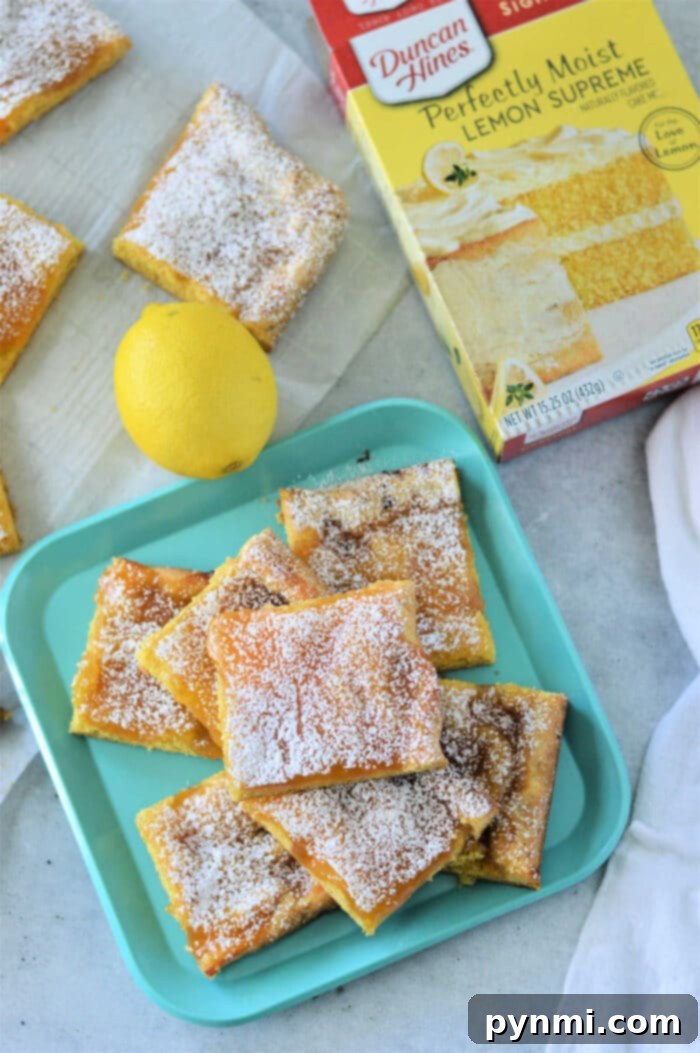 Lemon bars with cake mix dusted with powdered sugar rest elegantly on a blue tray, accompanied by a fresh lemon and the cake mix box for inspiration.