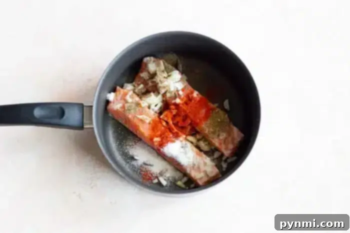 Delicate Poached Fish 4 Pieces of salmon gently simmering in a pan, topped with salt, pepper, chopped onion, and red spices, indicating a well-seasoned boiled fish preparation.
