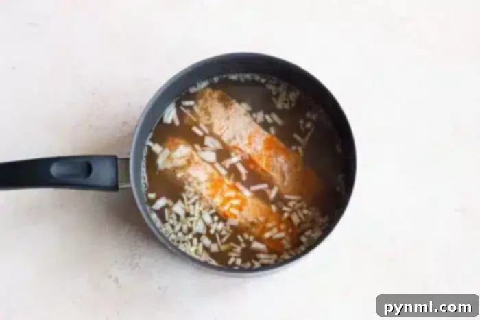 Delicate Poached Fish 5 A black saucepan containing fish fillets gently poached in a seasoned broth, garnished with chopped onions. The pan rests on a light-colored countertop, promising a delicious and comforting meal.