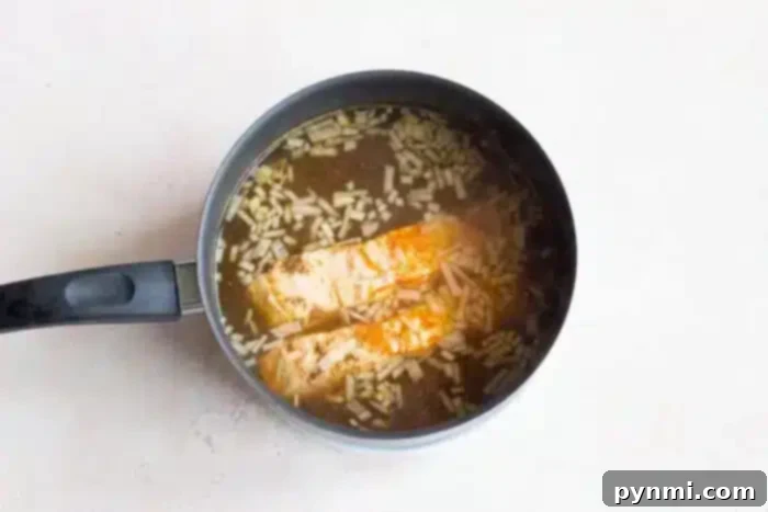Delicate Poached Fish 8 A saucepan on a light surface contains two pieces of gently boiled fish cooking in a broth with visible rice grains and rising steam, indicating it is being heated to perfection.