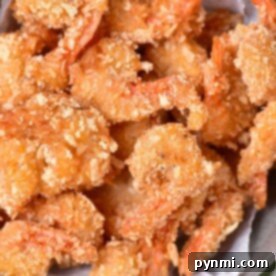A bowl of golden, crunchy coconut shrimp sits on parchment paper, perfectly fried to a crisp.