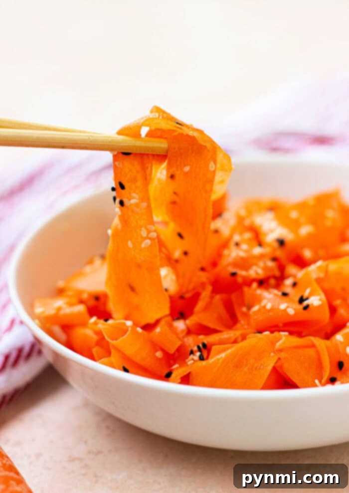 Chopsticks gracefully hold pieces of a delicious Raw Carrot Salad, sprinkled with sesame seeds, freshly lifted from a pristine white bowl.