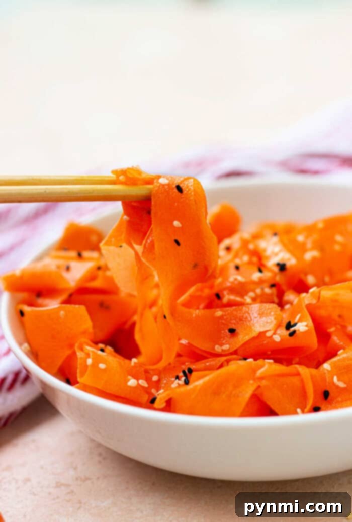 A bowl of raw carrot salad featuring delicate ribbons sprinkled with sesame seeds, gracefully lifted with chopsticks.