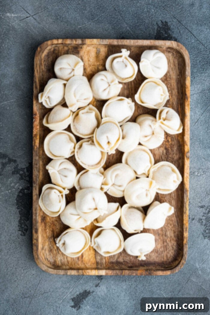 From Freezer to Feast: Creative Tortellini Creations 3 A wooden tray filled with uncooked dumplings on a textured gray surface, perfect inspiration for those exploring Crockpot Recipes with Tortellini.