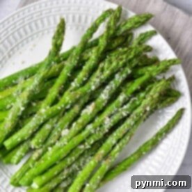 A plate of Ninja Foodi-cooked asparagus spears, perfectly garnished with grated cheese, sits elegantly on a white plate.