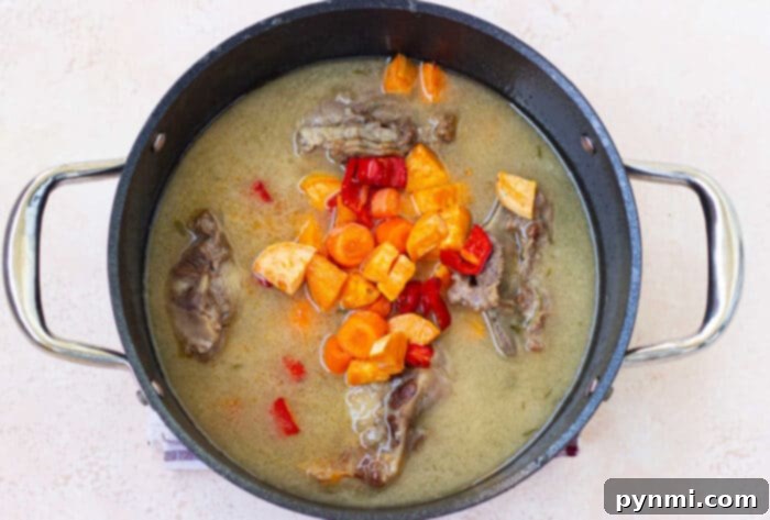 A pot of soup with tender beef ox tails, carrots, red peppers, and rich broth sits invitingly on a light background—a delightful hint for an easy oxtail recipe.