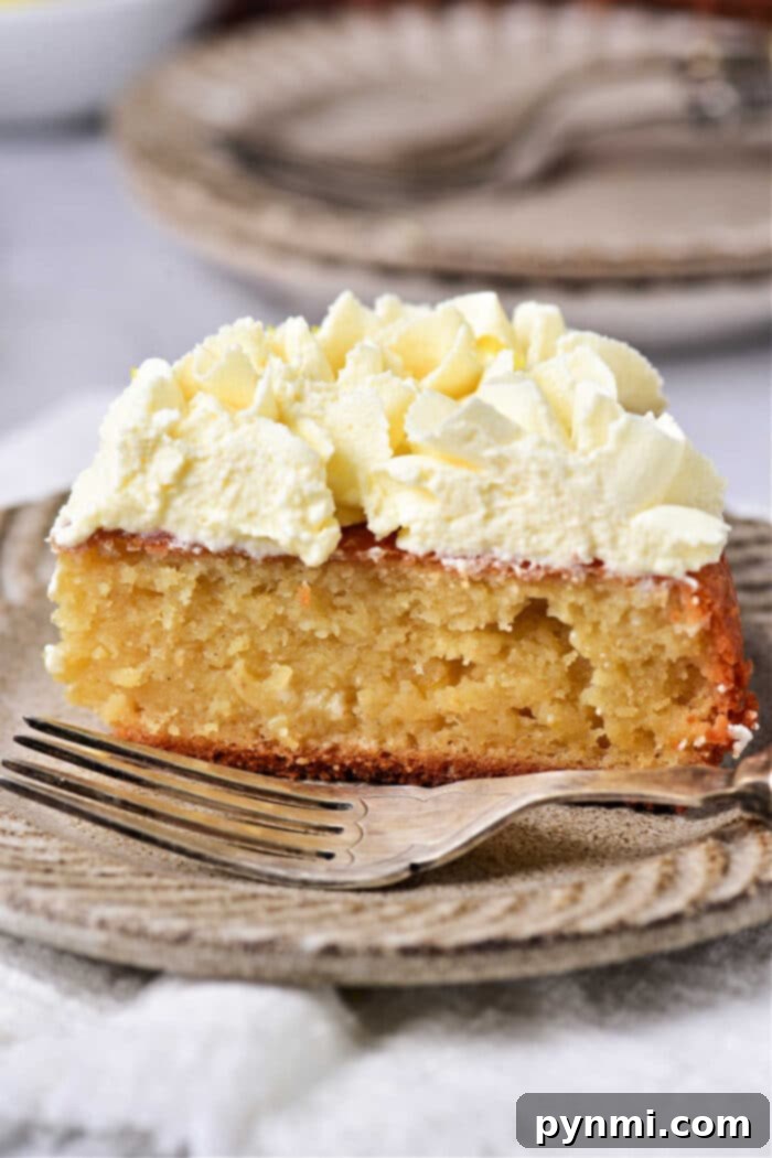 A slice of lemon cake with whipped cream and lemon curd on a rustic plate, accompanied by a fork.
