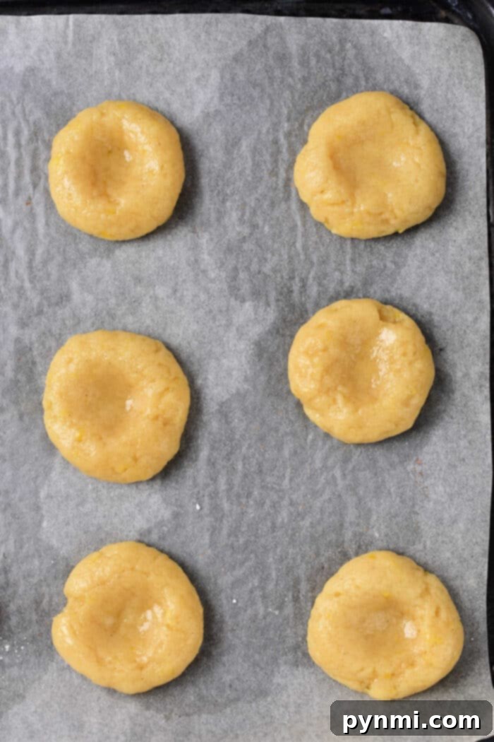 A close-up of beautifully baked Lemon Curd Thumbprint Cookies, showcasing the deep indentation and glossy curd.