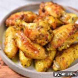 A plate of golden-brown air fryer honey lemon pepper wings is beautifully arranged on a wooden board. A small bowl of sauce sits invitingly in the background, complementing the savory delight.