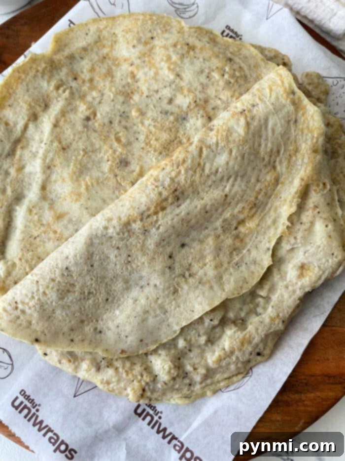A stack of golden egg white tortillas rests elegantly on branded parchment paper atop a rustic wooden surface, inviting you to create healthy meals.