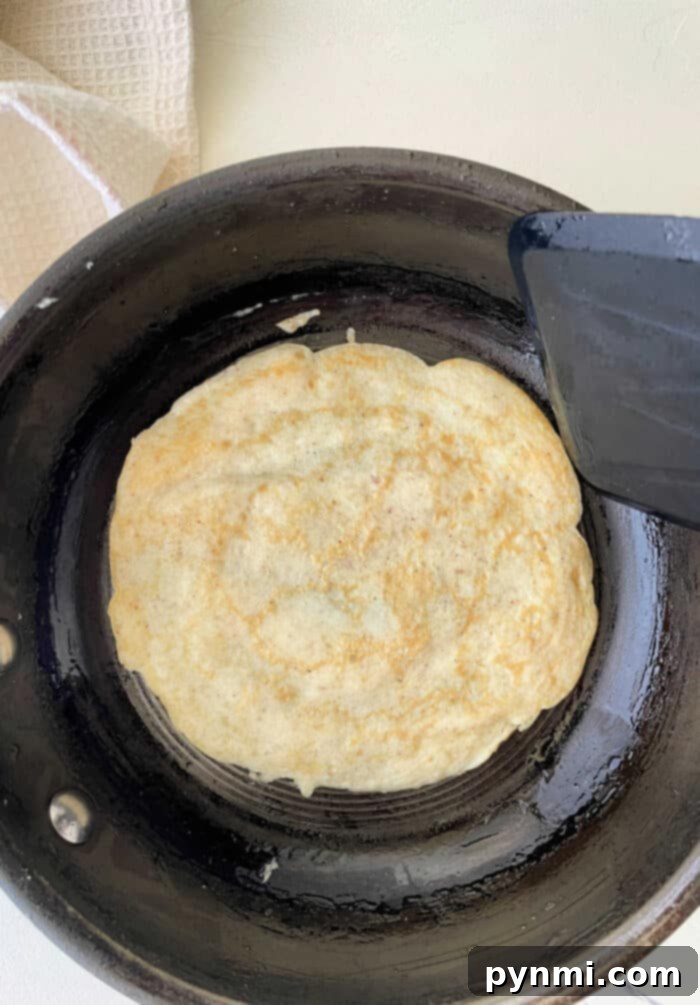 A golden brown egg white tortilla, perfectly circular, rests on a skillet, its edges crisp, ready to be filled with savory or sweet ingredients.
