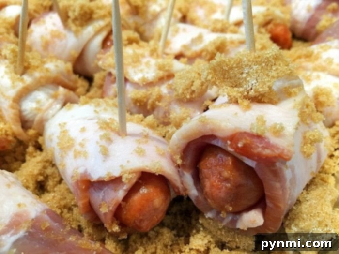Great salty and sweet appetizers with bacon that are great for super bowl parties, get togethers or as a side dish. The best recipe for cocktail wieners. #bacon #smokies #sweet #brownsugar #hotdogs #best #appetizers #wieners Close-up of perfectly wrapped bacon-wrapped hot dogs, secured with toothpicks and glistening with brown sugar, ready to bake.