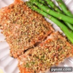Almond crusted salmon fillets with asparagus rest elegantly on a white plate, placed on a cheerful yellow cloth.