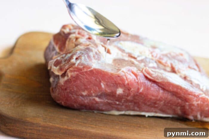 Achieving the Perfect New York Strip Roast 3 A spoon drizzling oil onto a raw New York Strip Roast on a wooden cutting board