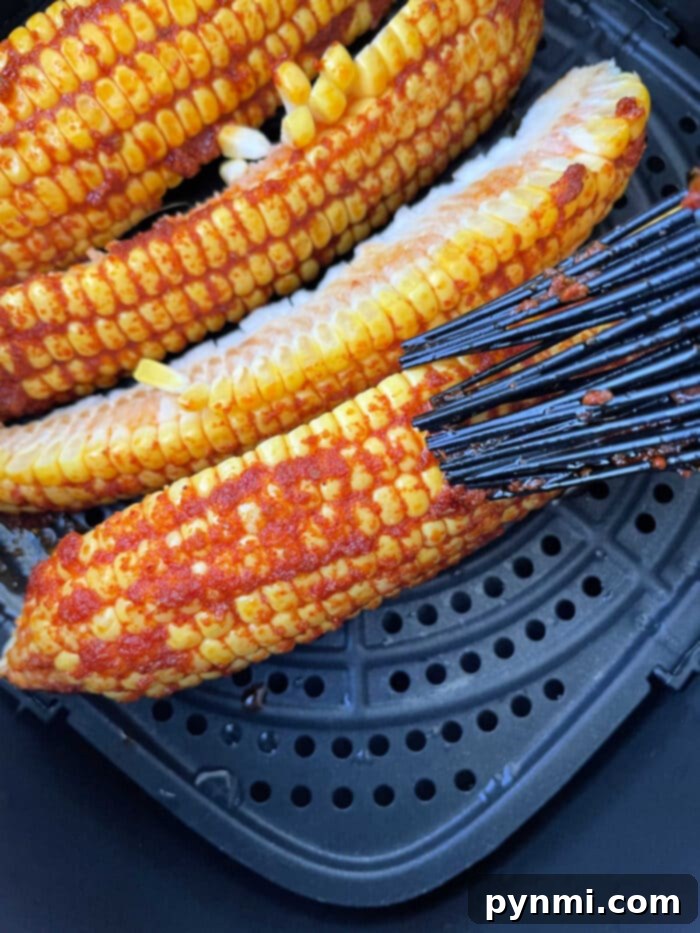Crispy Corn Ribs 5 Corn on the cob ribs, brushed with vibrant red seasoning, transforms into a delicious corn ribs recipe as it cooks in a sleek black air fryer basket.