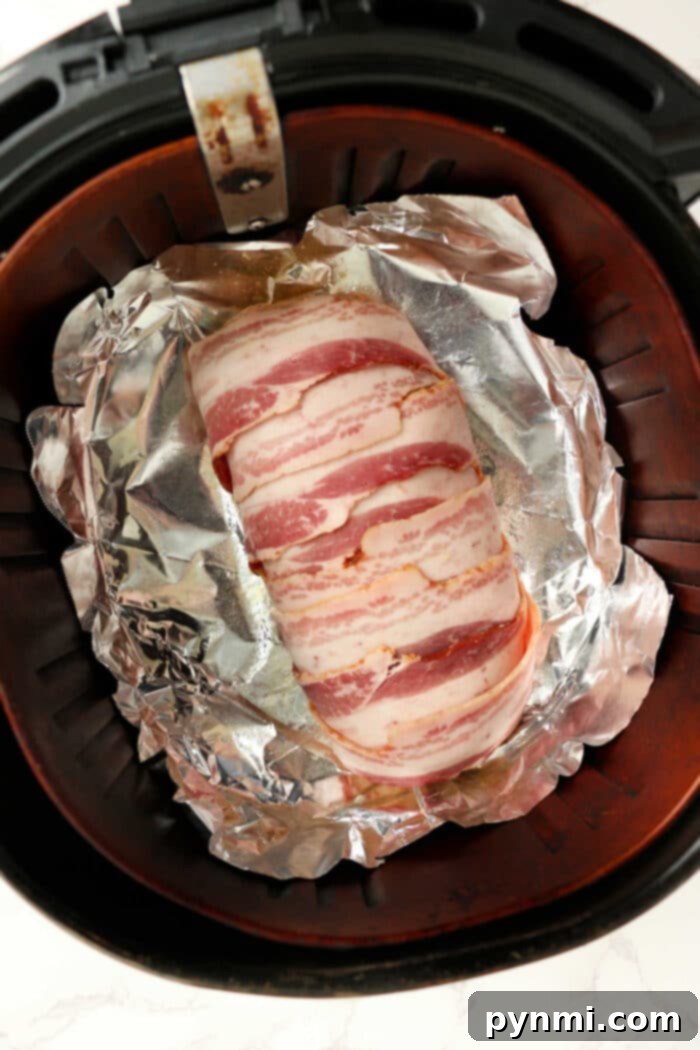 A perfectly cooked Air Fryer Bacon Wrapped Meatloaf, presented on a cutting board, ready to be sliced and served.