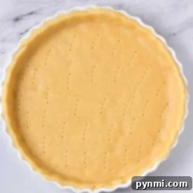Unbaked pie crust in a white tart pan, pierced with fork holes, ready for blind baking.