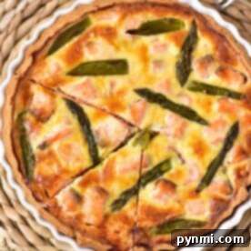A delicious salmon quiche recipe featuring a savory blend of salmon and asparagus in a white dish, cut into slices. Its elegantly presented on a woven placemat with two forks nearby, ready to delight your taste buds.