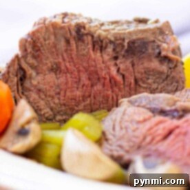 Close-up of a sliced Cross Rib Roast with tender carrots, potatoes, and mushrooms on a plate.