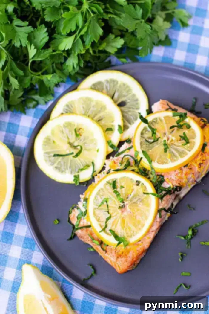Optimal Salmon Baking Time 350 2 A plate containing a piece of cooked salmon topped with lemon slices and chopped green herbs.