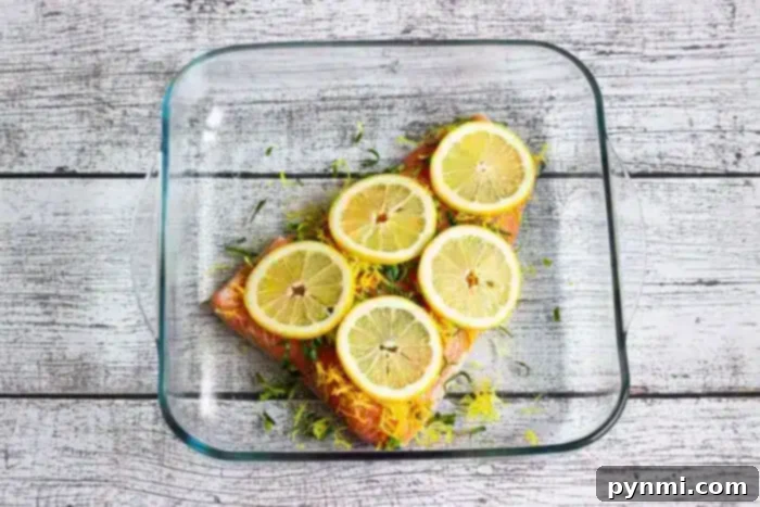 Optimal Salmon Baking Time 350 5 A glass baking dish contains a piece of salmon fillet topped with lemon slices and herbs.