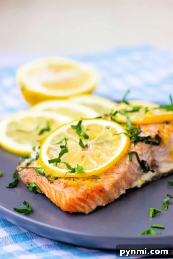 Optimal Salmon Baking Time 350 6 A piece of baked salmon garnished with lemon slices and chopped herbs is on a dark plate.