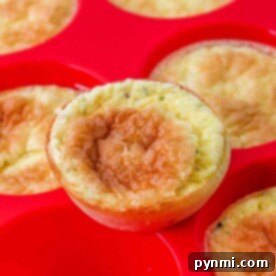 Close-up of crustless mini quiche muffins in a red silicone baking tray, one muffin slightly raised above the others.