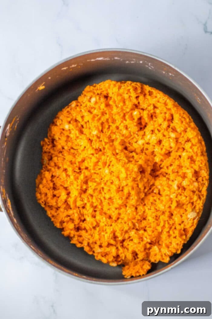 A pan filled with bright orange marshmallow cereal treats is positioned on a marble surface, reminiscent of Halloween Rice Krispie Treats.