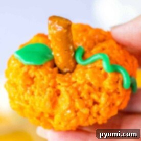 Orange Rice Krispie treat shaped like a pumpkin, complete with a pretzel stick stem and green icing leaf and vine, makes for the perfect Halloween delight.